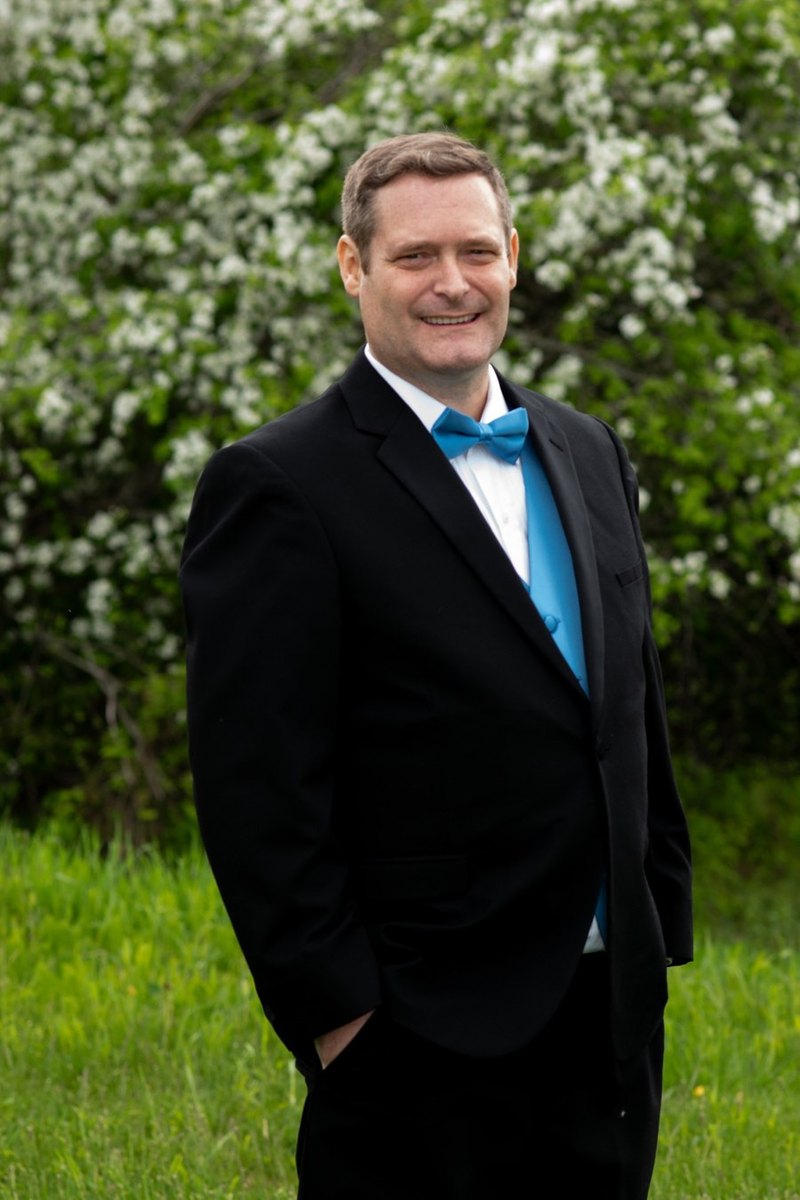 Bradley Saucier standing outdoors in a black suit and blue bow tie.